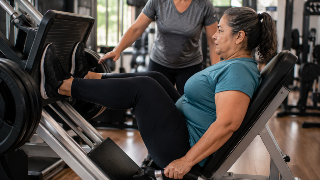 Mulher na pós-menopausa realizando exercício de leg press durante treinamento de força.